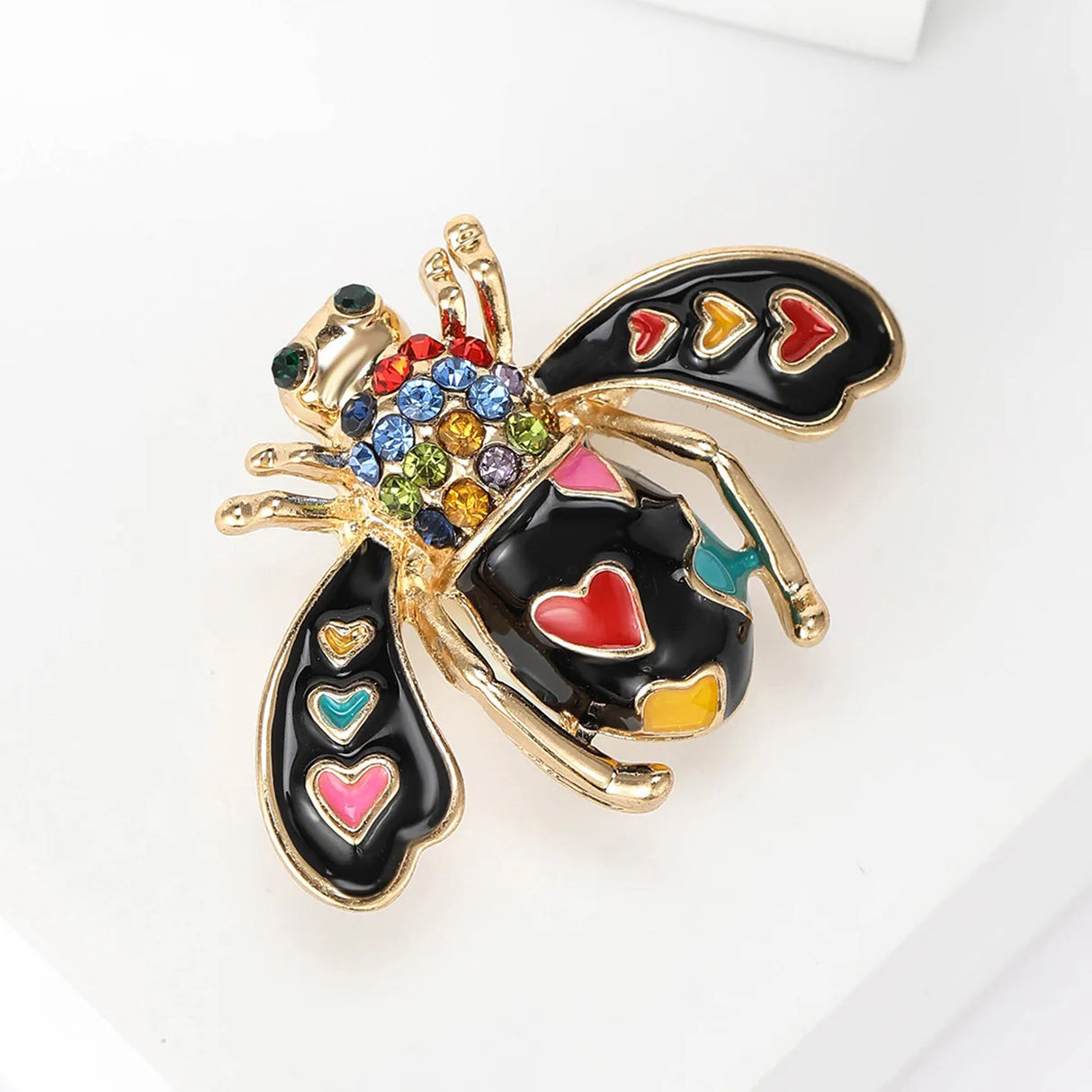 Bee brooch with black wings, multicolor heart details, clear faceted stones, and gold-tone finish, angled view.