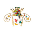 Bee brooch in white enamel with gold-tone frame, rainbow heart inlays, and multicolor faceted stones, cutout on white.