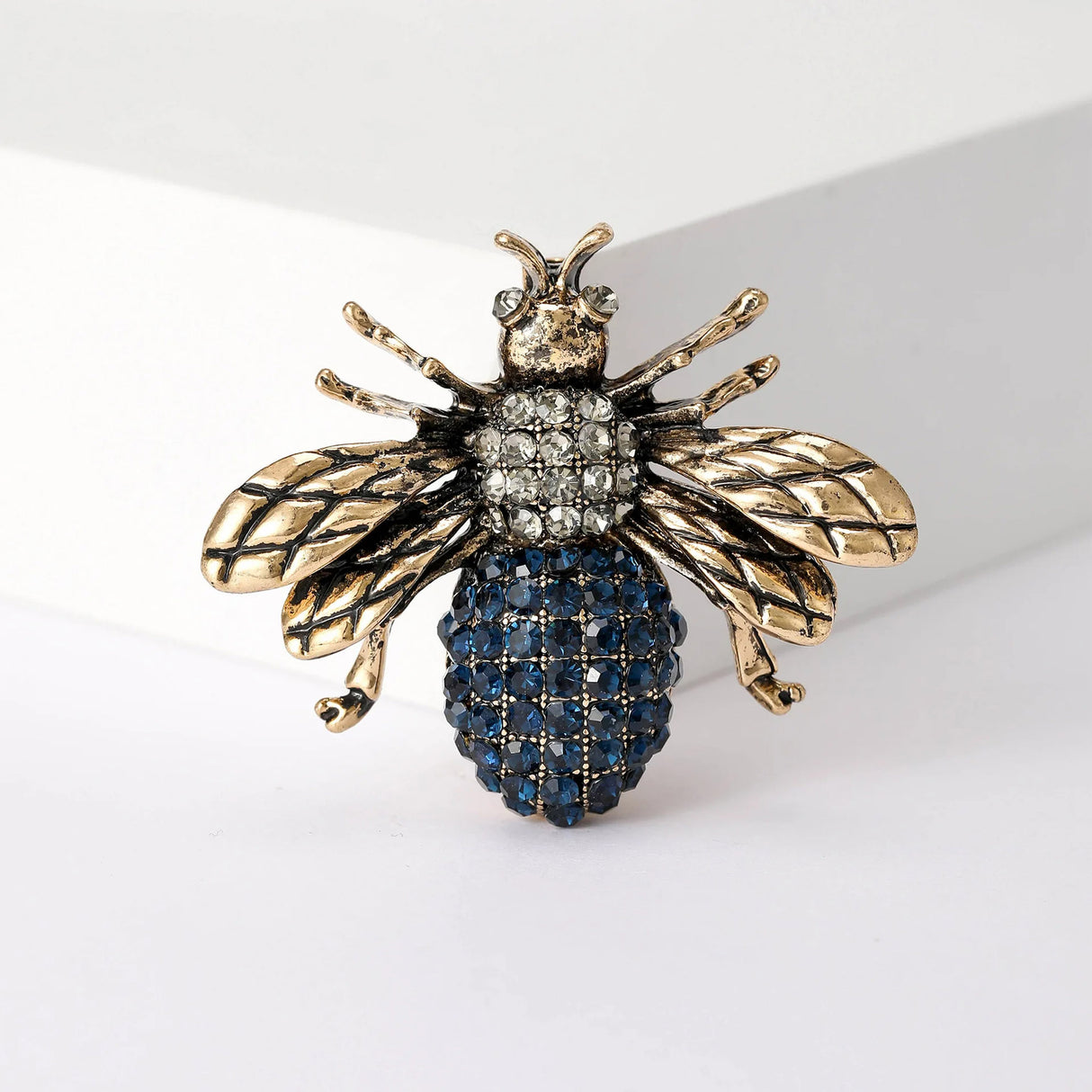 Bee brooch with gold-tone wings, clear faceted stone thorax, and blue stone bottom, upright studio pose.