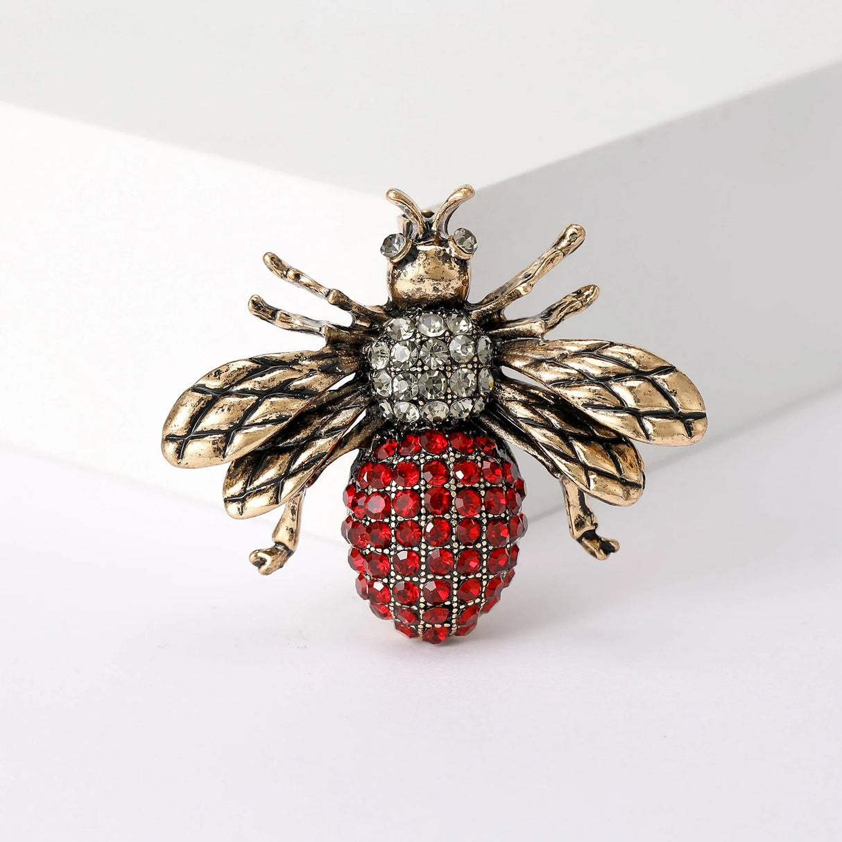 Bee brooch with gold-tone textured wings, clear thorax stones, and red faceted stone abdomen, upright studio pose.