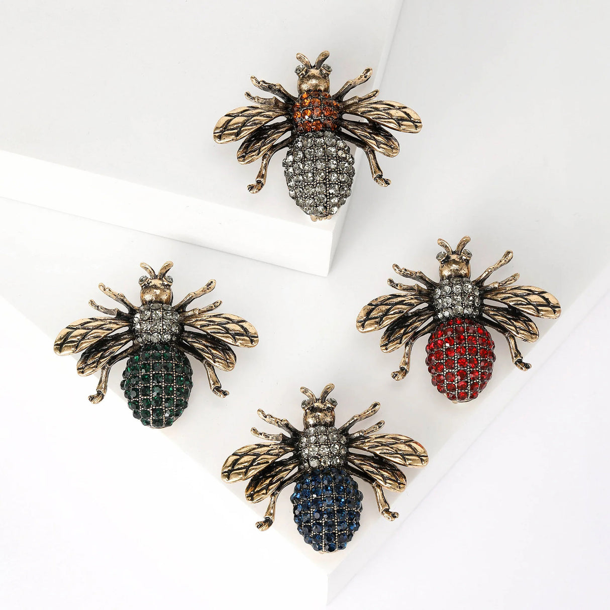 Set of four bee brooches with vintage-style gold-tone wings and multicolor faceted stone bodies in red, green, blue, and orange, flat lay on white.