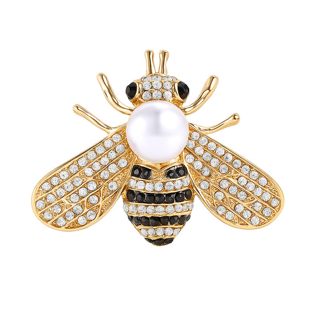 Bee brooch in gold-tone metal with clear stones, black striped details, and white round bead, cutout on white background.