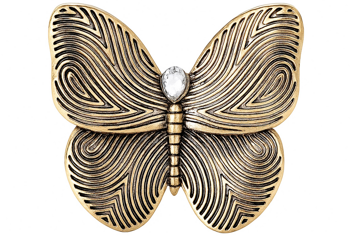 Butterfly brooch with gold-tone finish, black etched swirl wings, and clear teardrop stone, cutout on white. Landscape crop for secondary use.