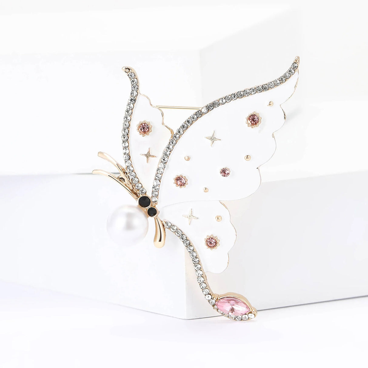 Butterfly brooch with white-tone wings, pink stones, pearl body, and star motifs, upright pose on white block.