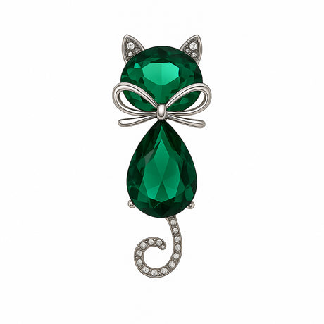 Cat brooch with green faceted stones, silver-tone bow detail, and spiral tail adorned with clear stones, cutout on white.