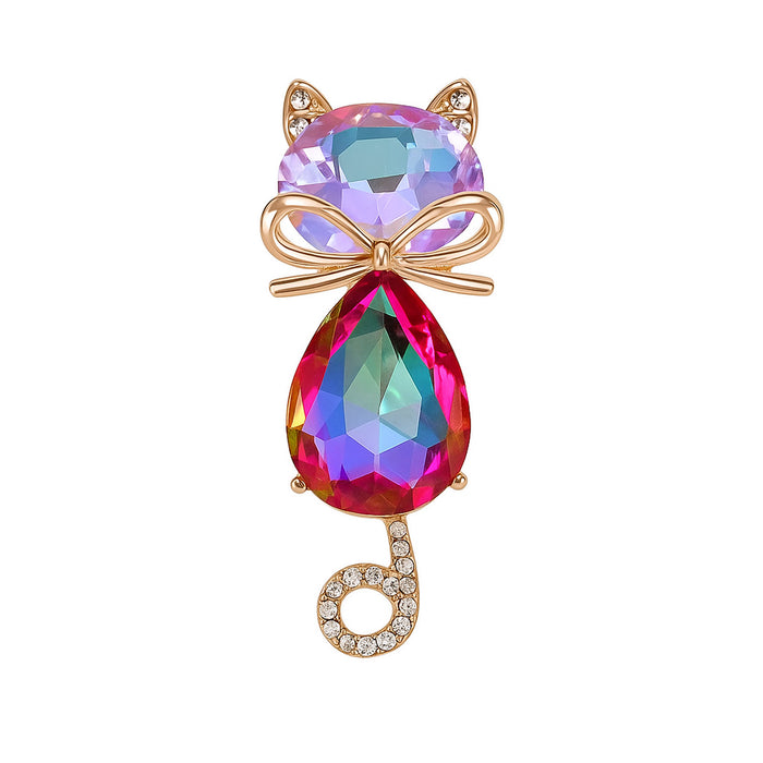 Cat brooch with iridescent pink-purple faceted stones, gold-tone bow accent, and curled tail with clear stones, cutout on white.