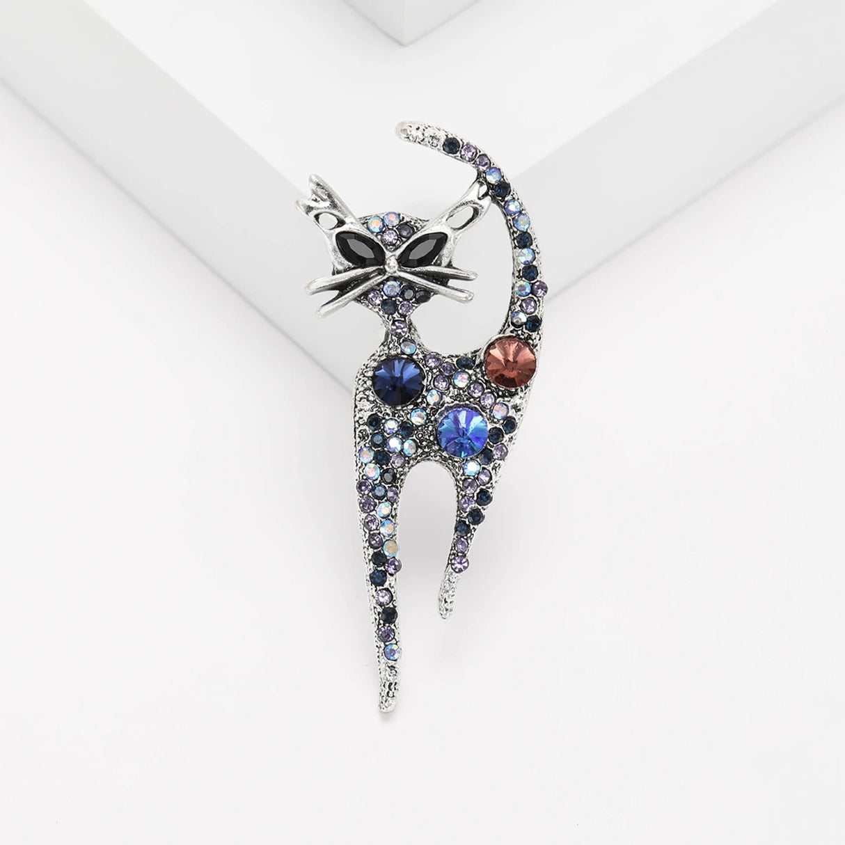 Cat brooch with antique-inspired silver-tone base and round blue stones with a red accent, displayed on white studio platform.