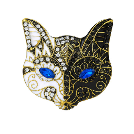 Cat mask brooch with black and white enamel finish, blue faceted eyes, clear and black stones, cutout on white background.