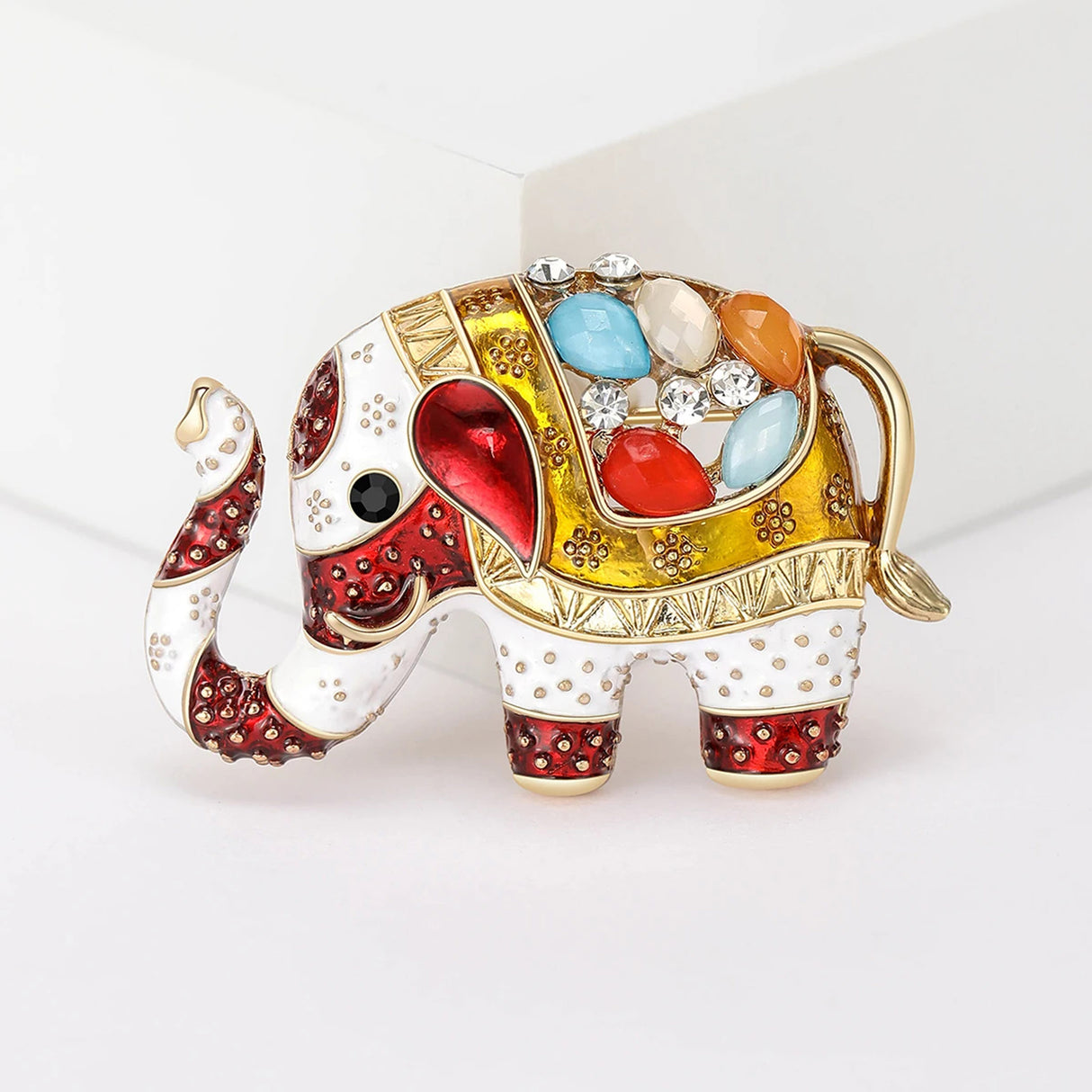 Elephant brooch in red and gold-tone enamel with white base, clear and multicolor stones, front studio view.