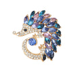Hedgehog brooch in gold-tone metal with clear faceted stones and marquise stones in blue and purple, cutout on white.