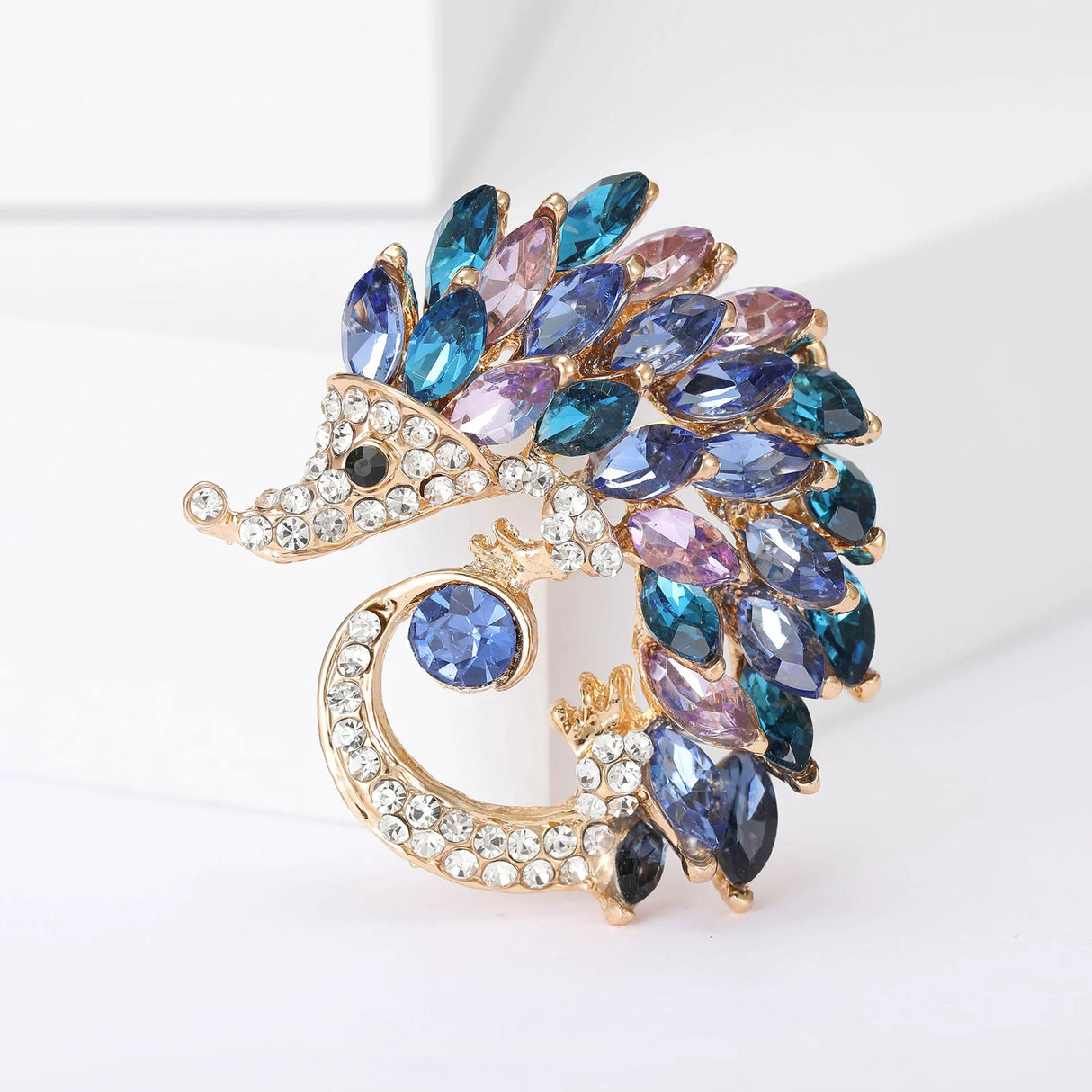 Hedgehog brooch with gold-tone base, clear pave-set stones, and blue, purple, and pink marquise stones, upright on white.