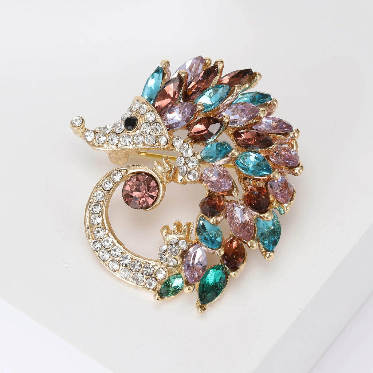 Hedgehog brooch with gold-tone metal, clear small pave stones, and multicolor bigger marquise stones in blue, pink, and brown, top-down view.