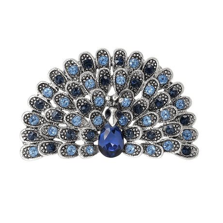Peacock brooch with light and dark blue faceted stones, silver-tone metal, and blue teardrop center stone, cutout on white.