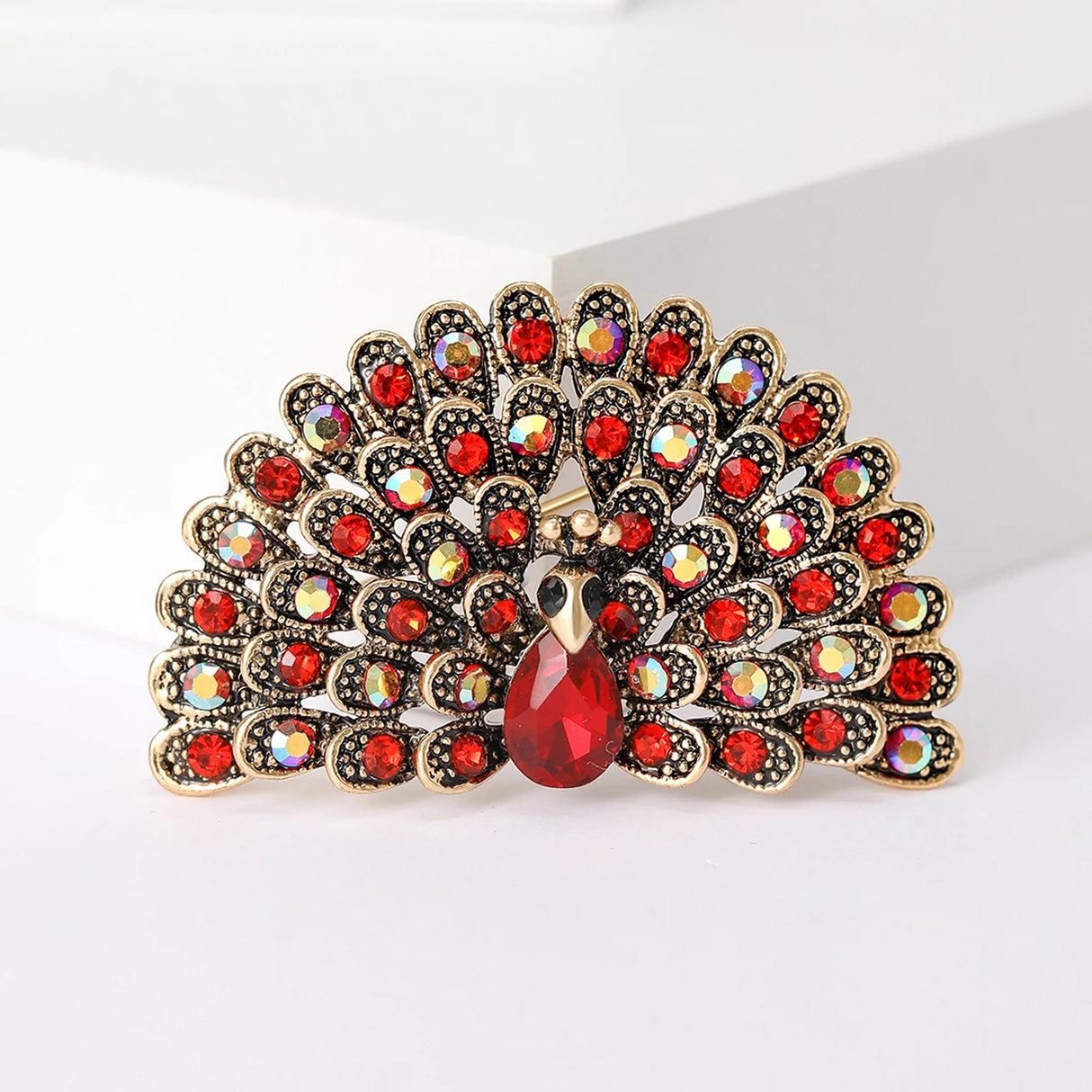 Peacock brooch with gold-tone metal, red and iridescent stones, and faceted red teardrop center, cutout studio view.