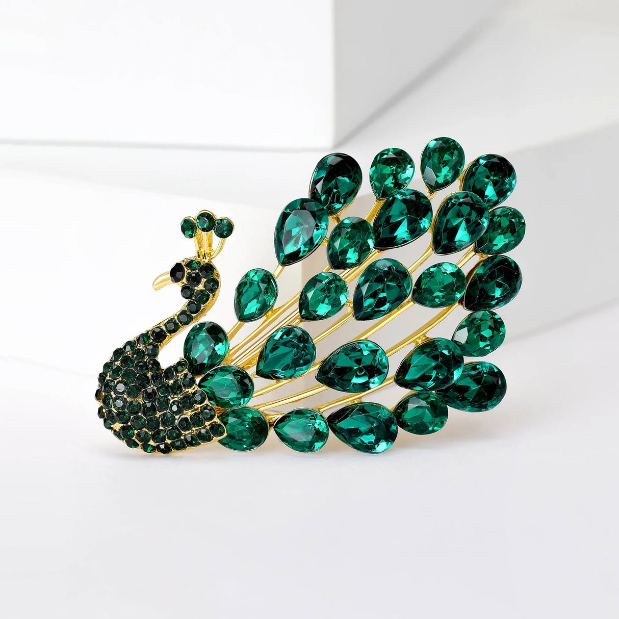 Peacock brooch with gold-tone metal, green teardrop faceted stones, and small round stones, upright view on white.
