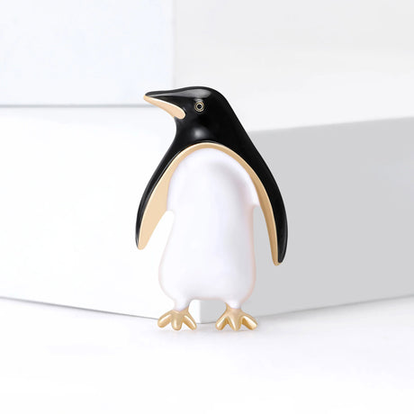 Penguin brooch with black enamel head and wings, white body, and gold-tone feet, standing pose on white surface.