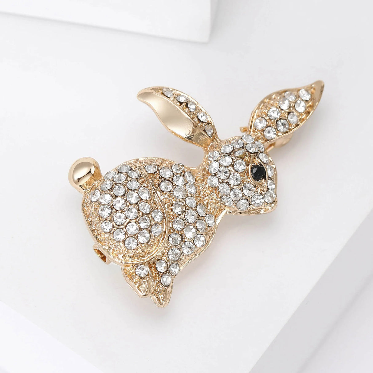 Bunny brooch with gold-tone metal, clear faceted stones, and black eye, angled view on white surface.