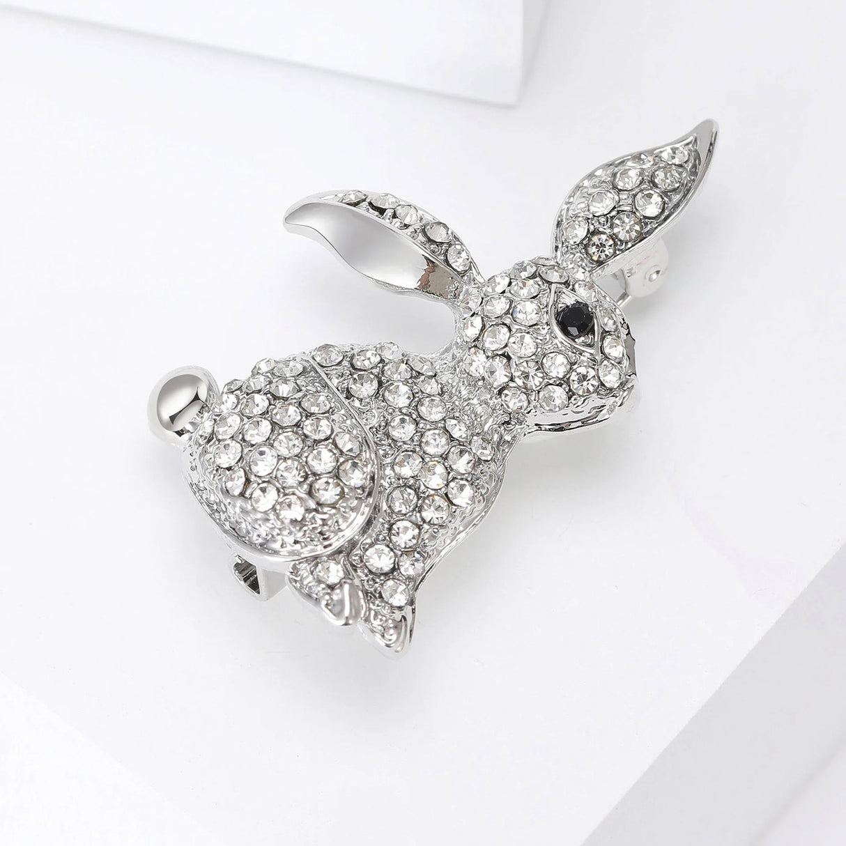 Bunny brooch in silver-tone finish with clear faceted stones and black eye, angled view on white surface.