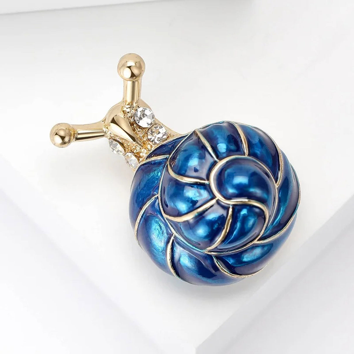 Snail brooch with blue-toned swirl shell, gold-tone metal and clear faceted stones, top-left angled view.