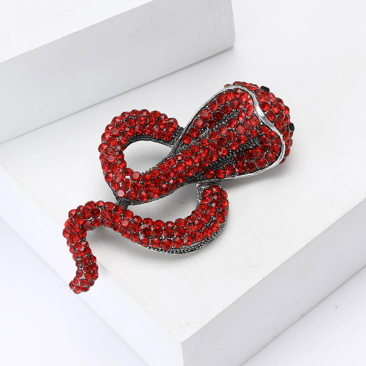 Snake brooch with red faceted stones and silver-toned metallic base, angled flat lay on white surface.