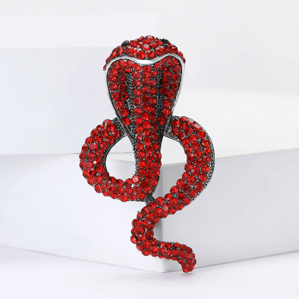Snake cobra brooch with red stones and silver-tone metal base, front view on white display block.