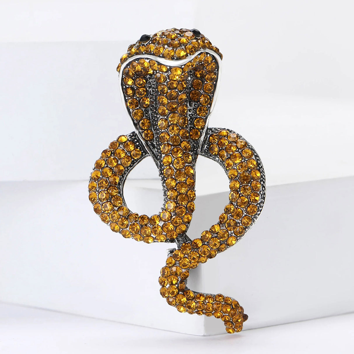 Cobra snake brooch with yellow faceted stones and silver-tone edging, upright pose on white step platform.
