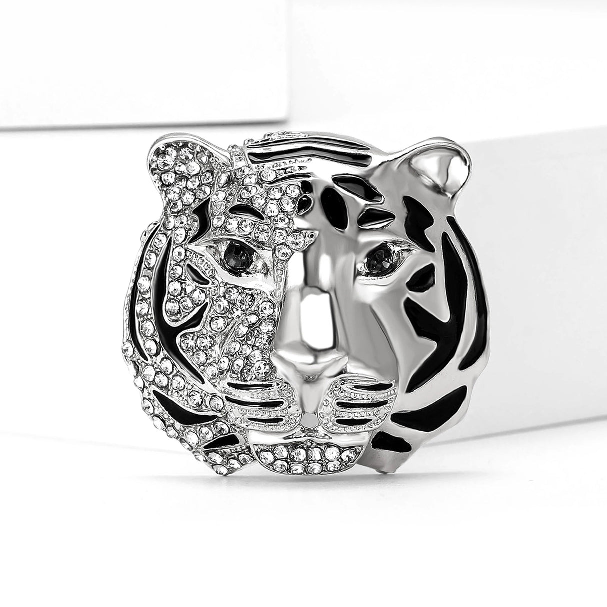 Tiger head brooch in silver-tone metal with partial clear stone detailing and black enamel stripes, upright on white platform.