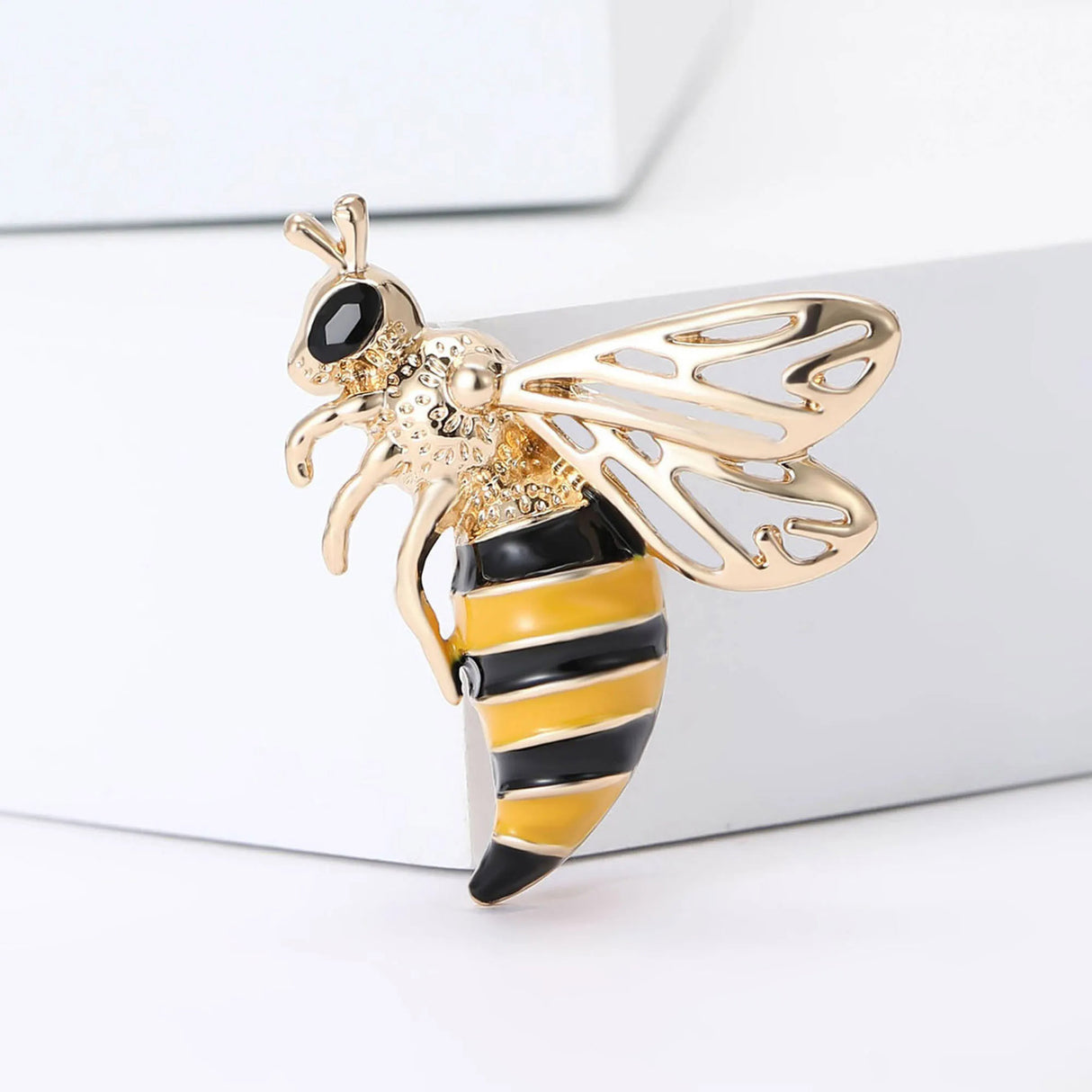 Wasp brooch with gold-tone metal, black and yellow striped body, openwork wings, and black faceted eye, cutout on white background.