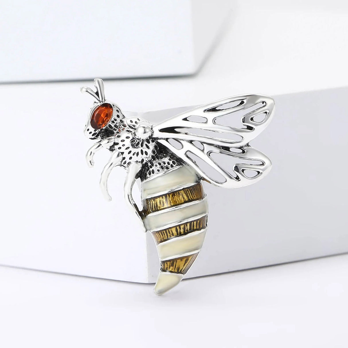 Wasp brooch with silver-tone metal, amber-toned eye, white and bronze striped body, and filigree wings, cutout on white background.