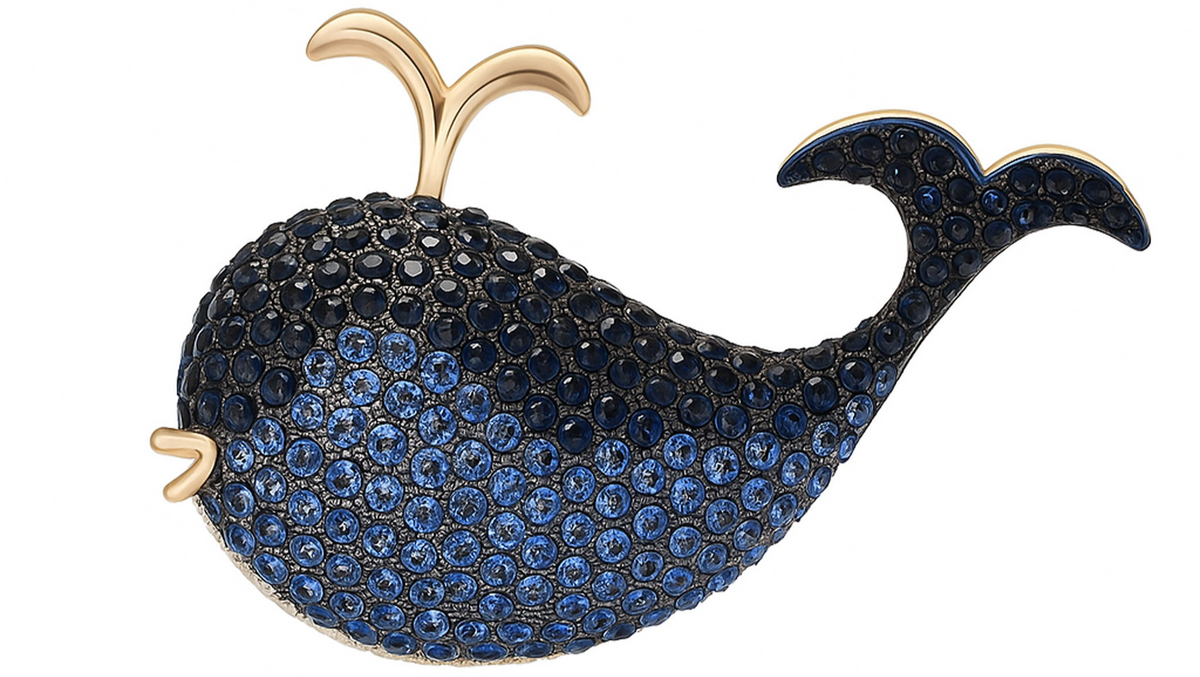 Whale brooch decorated with blue faceted pave stones and gold-tone spout, cutout on white background. Landscape crop for secondary use.