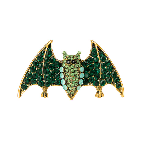 Bat brooch with gold-tone base, green faceted stones, light green center stones, and black eyes, cutout on white.