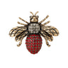 Bee brooch with antique gold-tone wings, clear stones on thorax, and red clustered stones on oval bottom part of body, cutout on white.