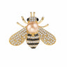 Bee brooch with gold-tone finish, clear faceted stones, black accents, and beig-pink round bead, cutout on white.