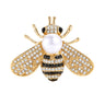 Bee brooch in gold-tone metal with clear stones, black striped details, and white round bead, cutout on white background.