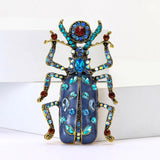 Beetle brooch featuring blue enamel body with gold-tone legs and blue and red stones on wings and antennae, upright front view.