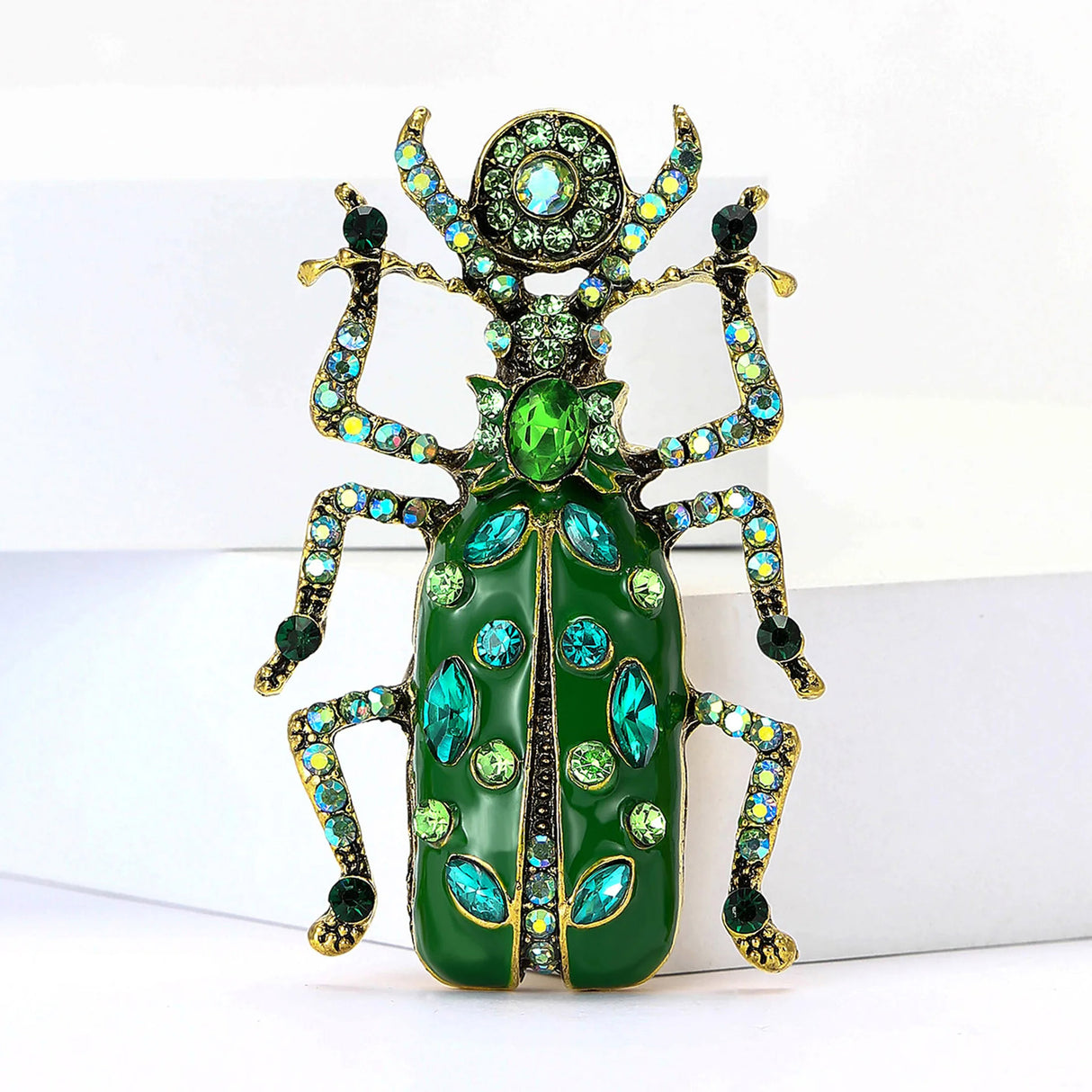 Beetle brooch with green body, gold-tone legs, and various shades of green-blue and iridescent stones on wings and limbs, upright front view.