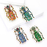 Set of four beetle brooches in assorted body colors with gold-tone limbs and multicolor decorative stones, flat lay on white.