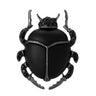 Beetle brooch with matte black body, dark metallic legs, and black faceted stones, cutout on white background.