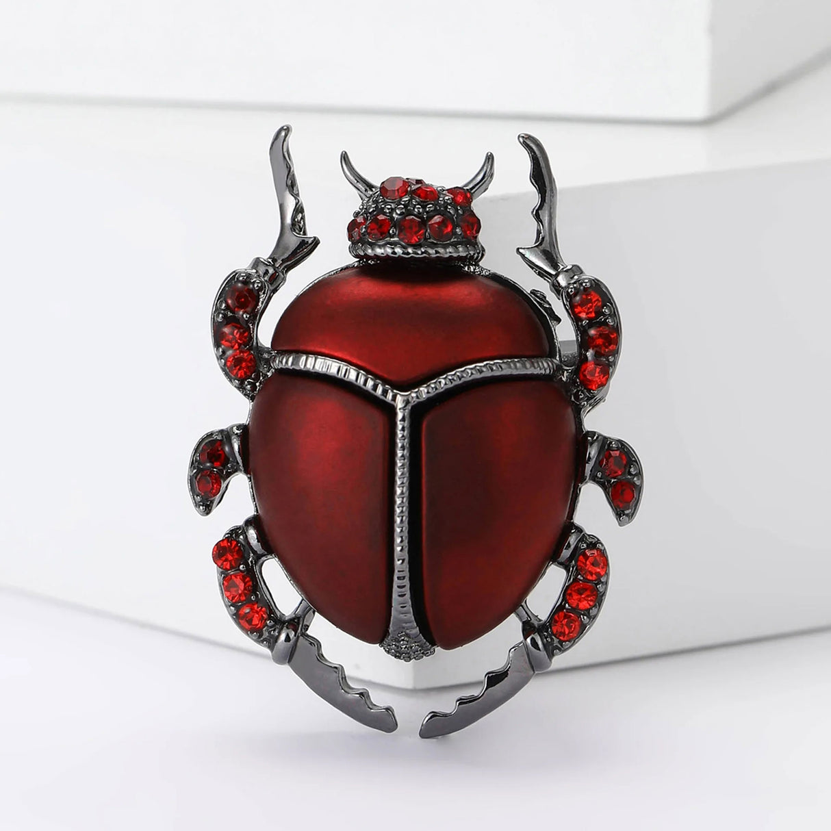 Beetle brooch with metallic red body, dark silver outline, and small round red stones, upright studio pose on white.