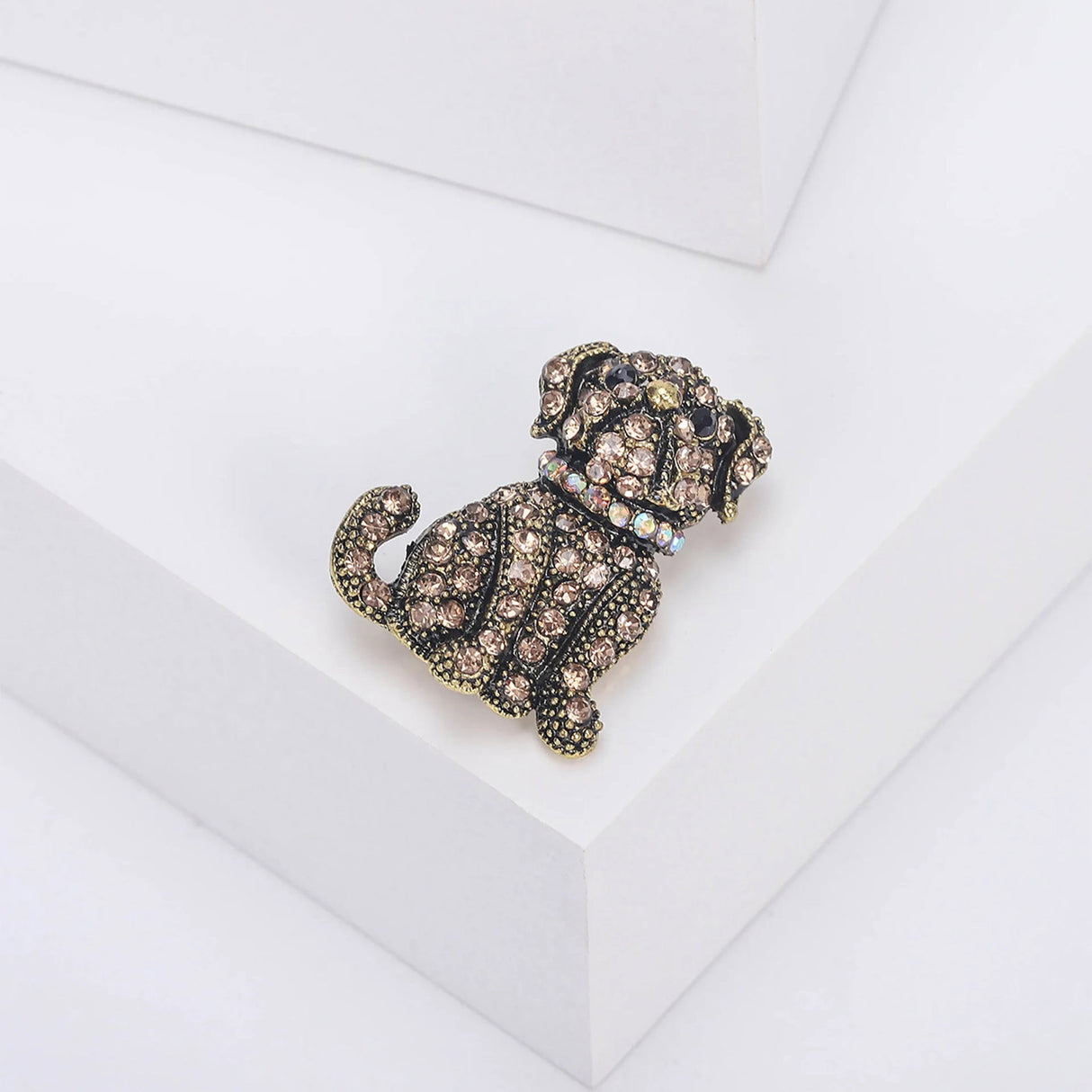 Bulldog brooch with brown faceted stones, black eyes, and iridescent collar on antique-style gold-tone metal, angled view on white block.