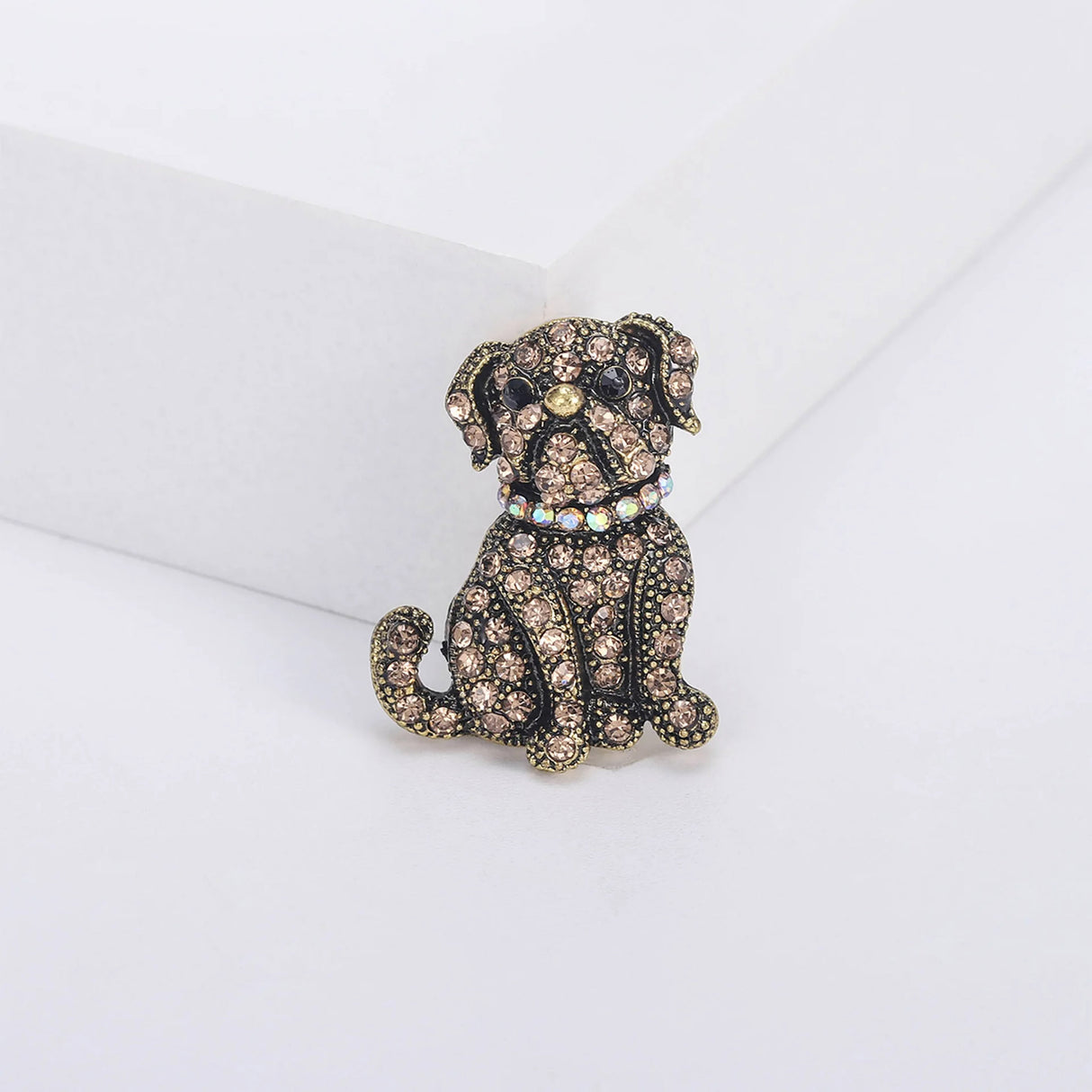 Bulldog brooch featuring brown faceted stones, black eyes, and iridescent collar on vintage-look gold-tone metal. Upright front view on white platform.