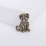Bulldog brooch featuring brown faceted stones, black eyes, and iridescent collar on vintage-look gold-tone metal. Upright front view on white platform.