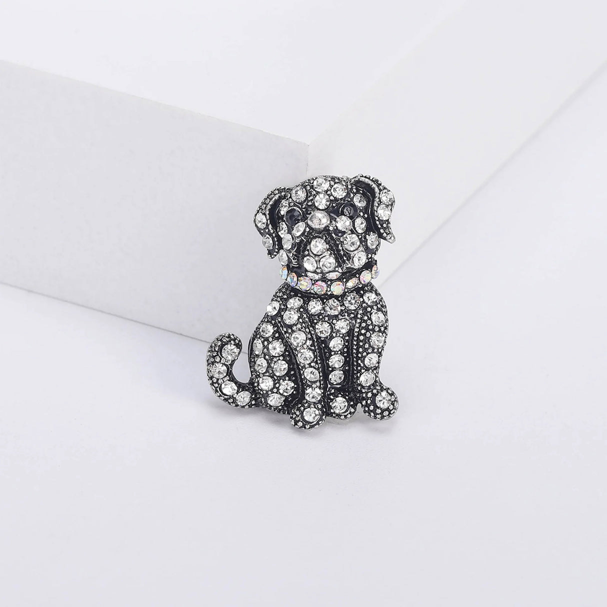Bulldog brooch with clear faceted stones, black eyes, and iridescent collar on vintage-look silver-tone metal, upright front view on white platform.