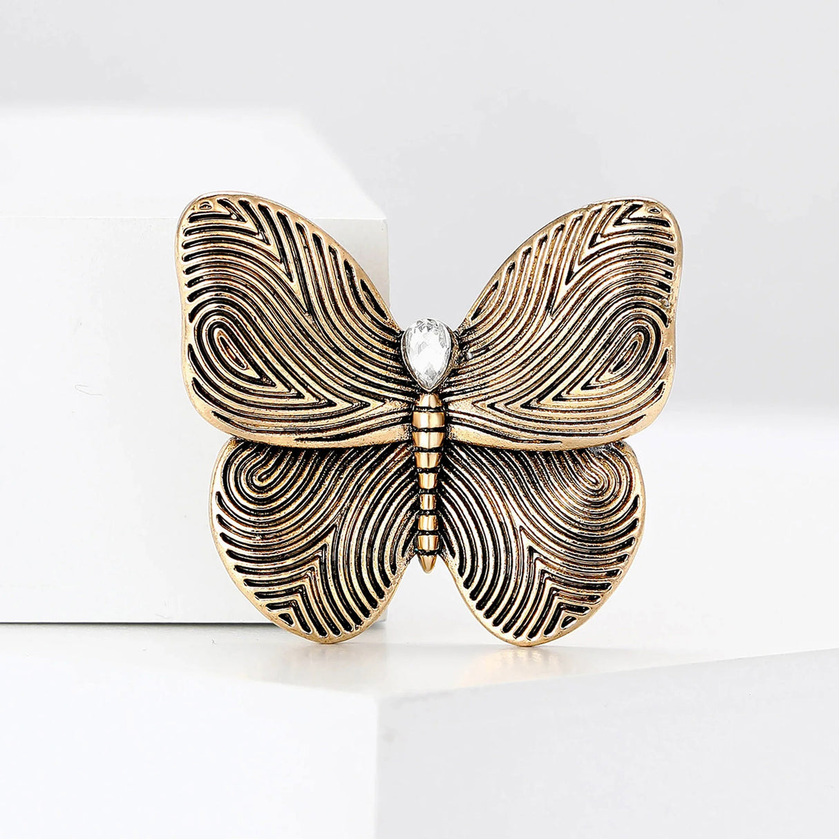 Butterfly brooch in gold-tone finish with black swirl wing patterns and a clear teardrop stone, upright studio pose.