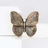 Butterfly brooch in gold-tone finish with black swirl wing patterns and a clear teardrop stone, upright studio pose.