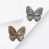Gold-tone and silver-tone butterfly brooches with swirl wing etching and clear teardrop stones, flat lay on white.