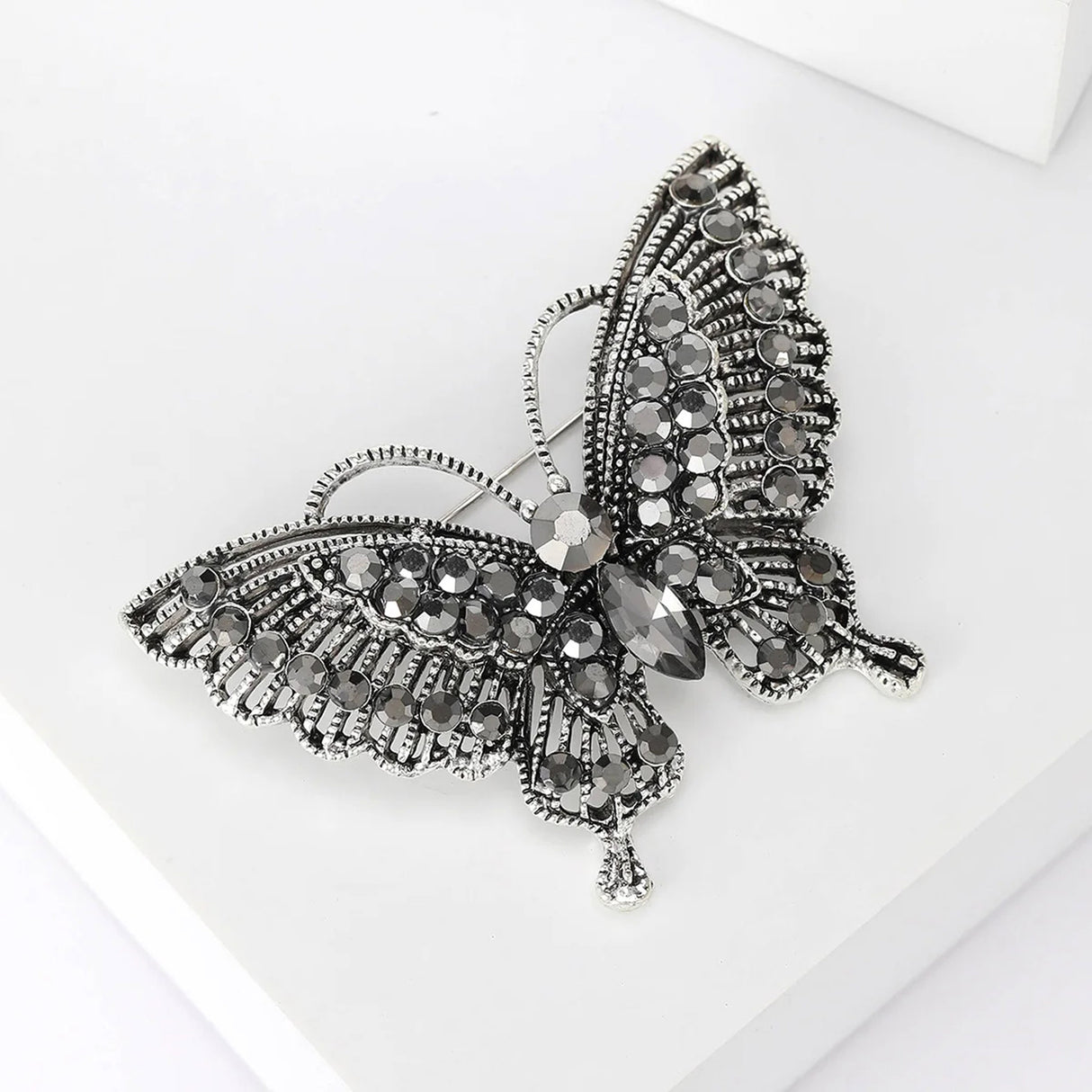 Butterfly brooch with silver-tone base, black faceted stones, and intricate wing detailing, angled view on white.