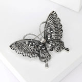 Butterfly brooch with silver-tone base, black faceted stones, and intricate wing detailing, angled view on white.