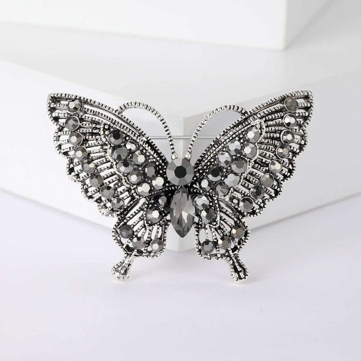 Butterfly brooch with dark silver-tone finish, black faceted stones, and textured wings, front view on white block.