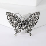 Butterfly brooch with dark silver-tone finish, black faceted stones, and textured wings, front view on white block.